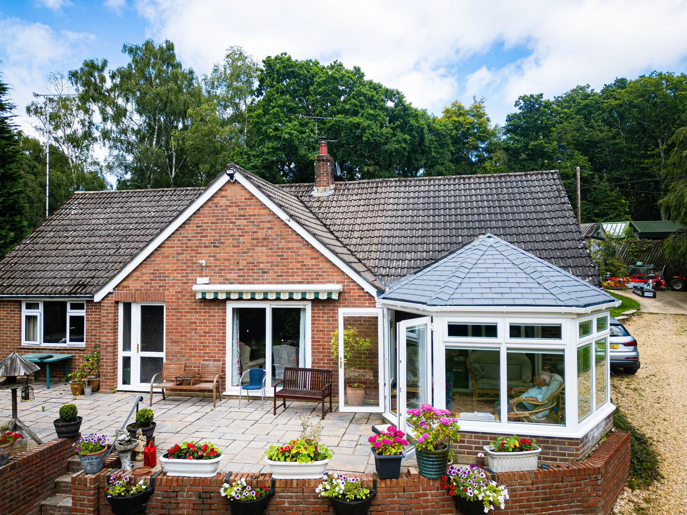 WarmerRoof tiled conservatory roof in grey tiles on a brick bungalow, seen across a planted patio.